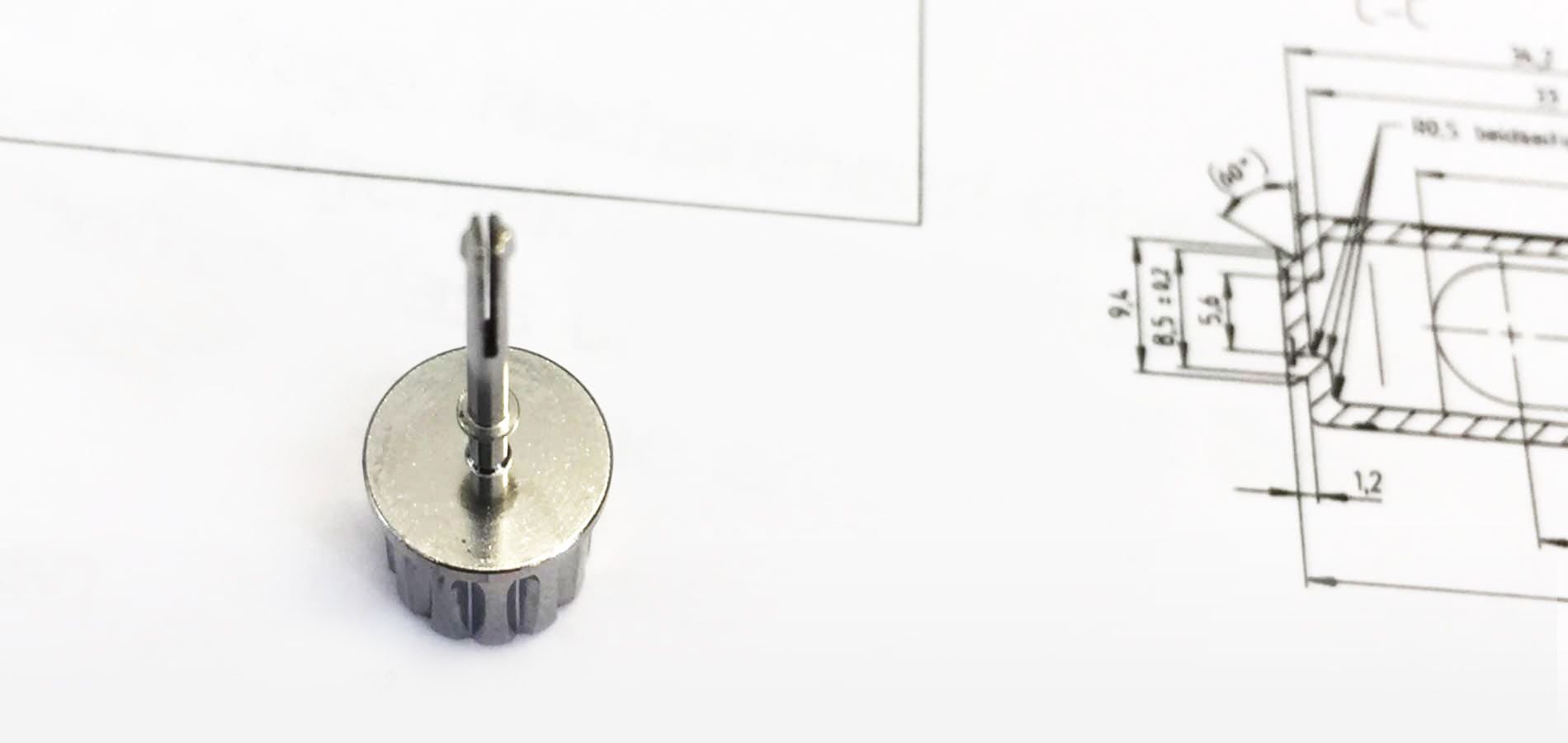 Eine Schraube liegt auf einem Bauplan, der technische Details und Maße zeigt.